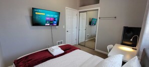 A hotel room with a bed, a TV mounted on the wall displaying a Roku TV interface, a mirror, and a bathroom with a sink and towel rack. - Easy access to I-5, Hwy 99. 1 bus stop from Aurora Transit Center. (Edmonds)