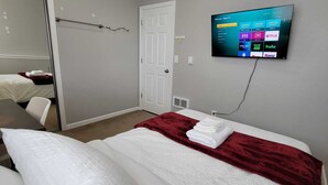 A hotel room with a bed, a TV mounted on the wall displaying a streaming service interface, and a door with a towel rack beside it. - Easy access to I-5, Hwy 99. 1 bus stop from Aurora Transit Center. (Edmonds)
