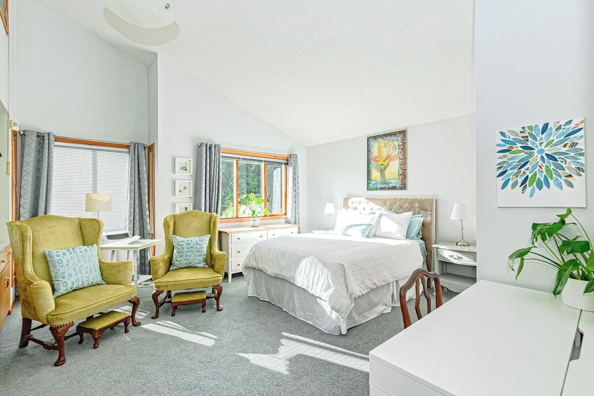 A bedroom with a bed, two armchairs, a desk, and a nightstand.