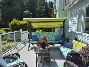 A covered patio with a swing seat, wicker furniture, and potted plants. - Bayview Bed and Breakfast (Mill Bay)