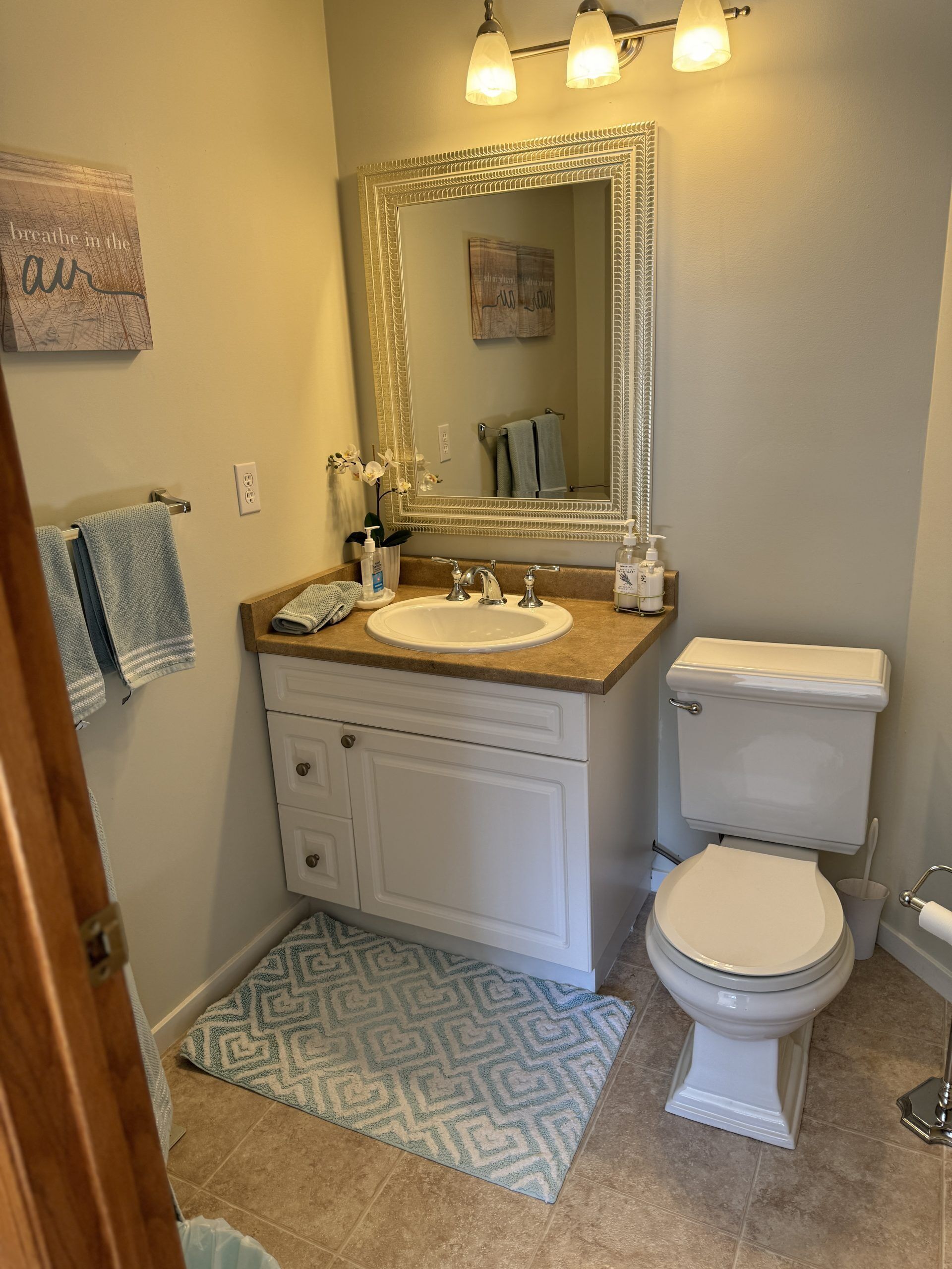 A bathroom with a white sink, vanity, and toilet. There is a mirror above the sink and a towel rack on the wall.