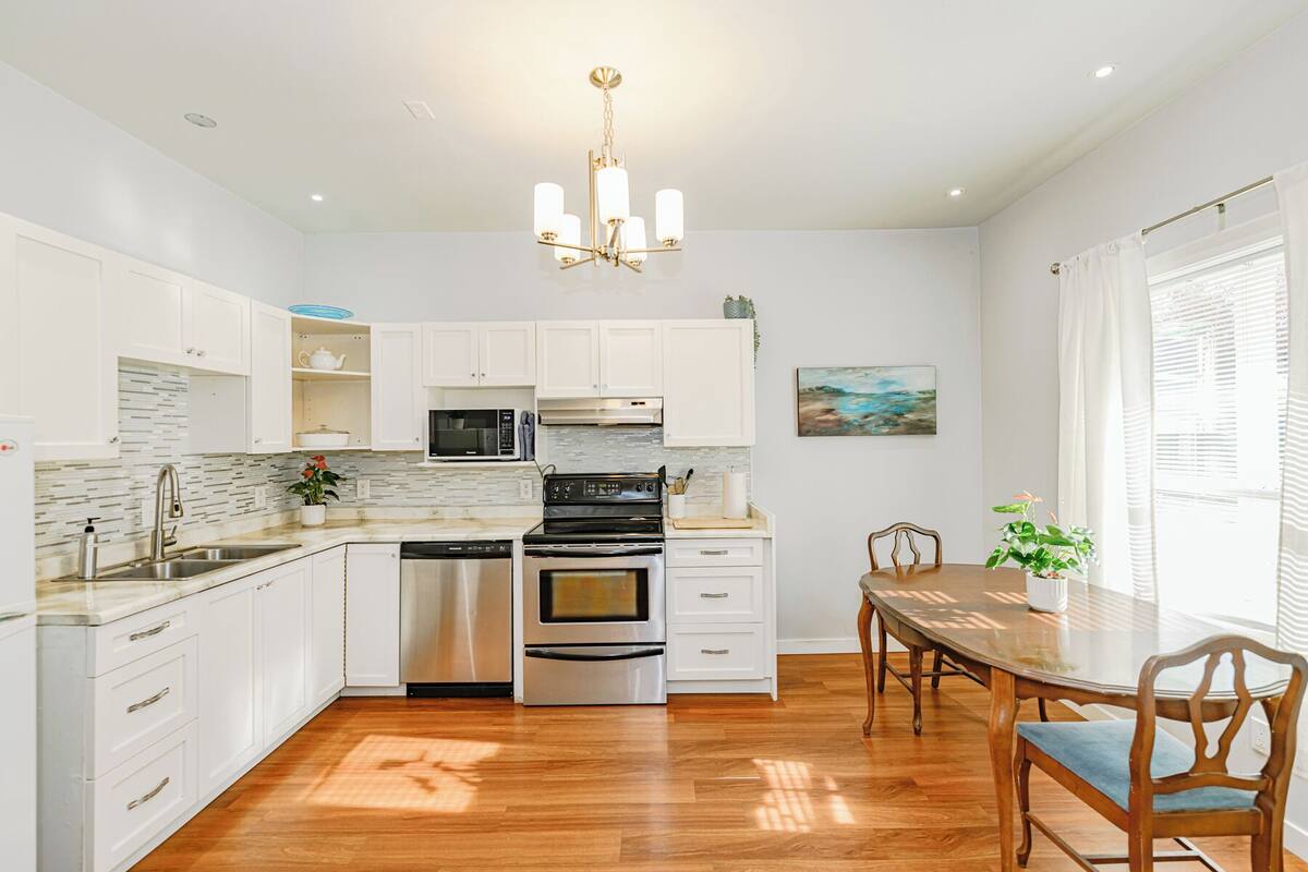 A modern kitchen with white cabinets, stainless steel appliances, and a wooden dining table with chairs.
