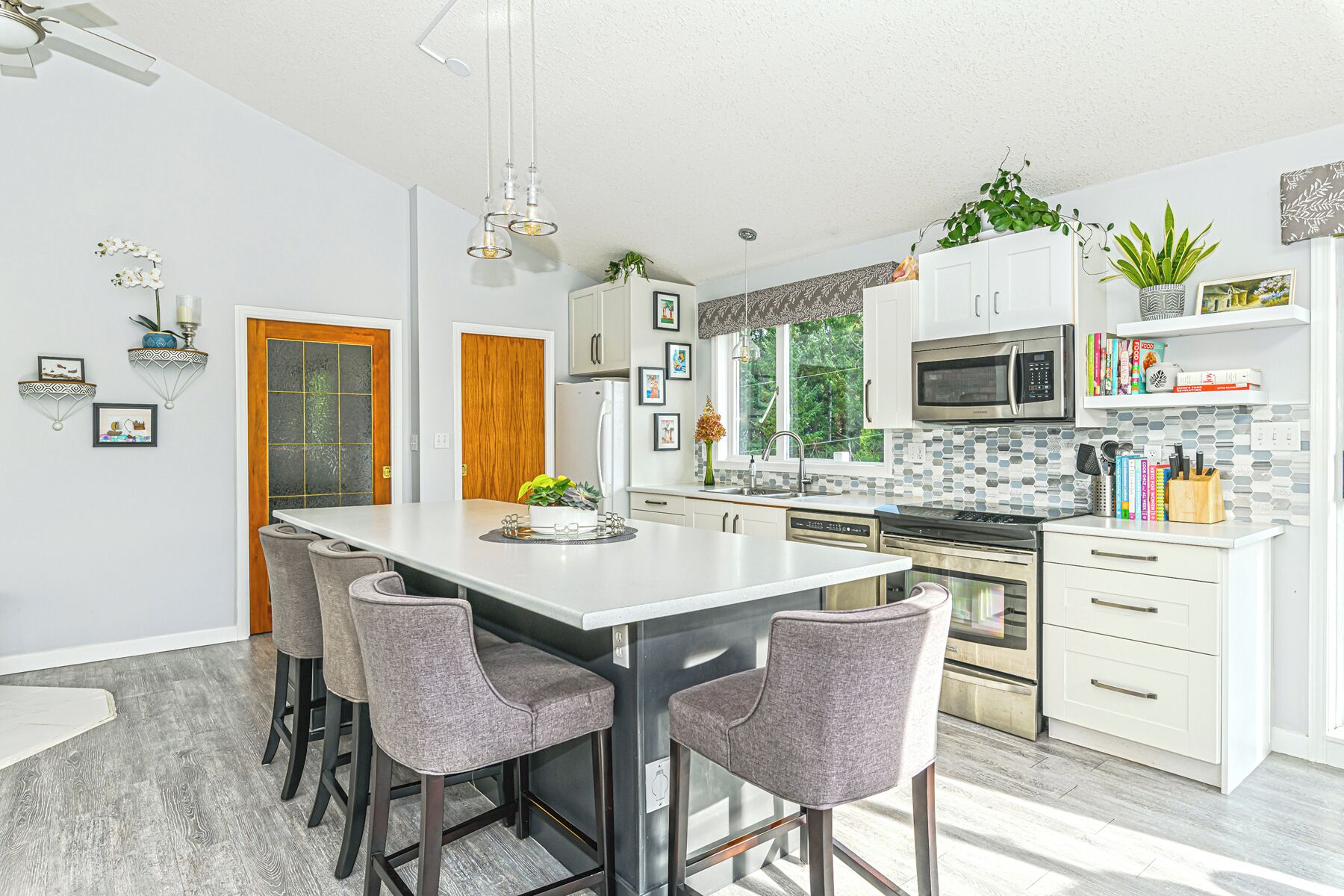 Cozinha moderna com ilha central, banquetas, eletrodomésticos de aço inoxidável e plantas decorativas.