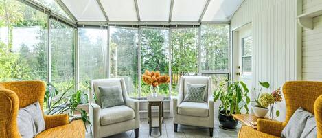 A conservatory with wicker chairs, a small table, and potted plants.