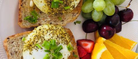 A plate with two slices of toast topped with poached eggs, garnished with herbs, and accompanied by a mix of grapes, cherries, strawberries, and orange slices.