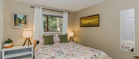 A bedroom with a bed, two bedside tables, a window with curtains, a ceiling light, and two framed pictures on the walls.