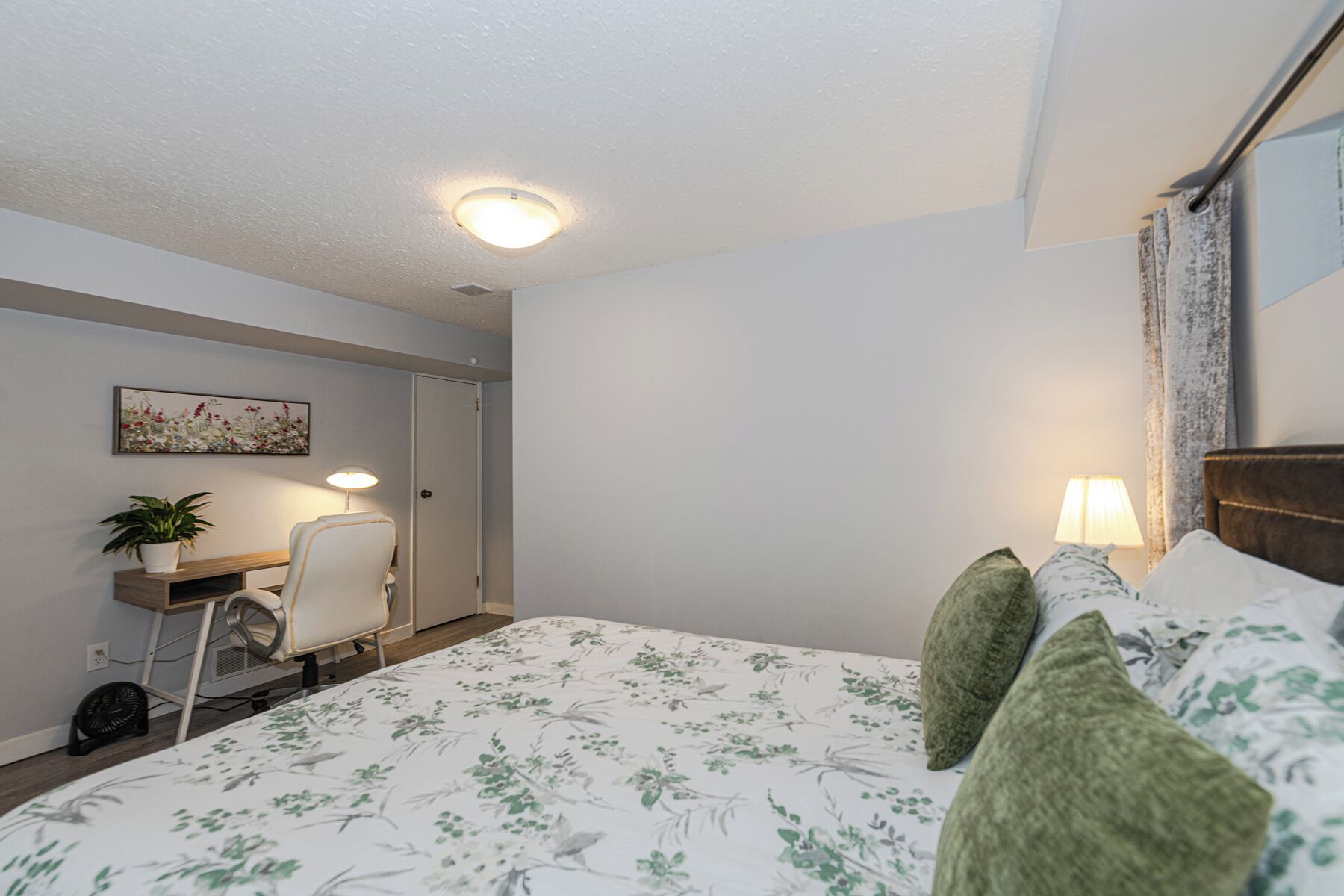 A bedroom with a bed, a desk, a chair, a lamp, and a ceiling light.