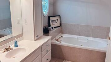 A bathroom with a white vanity, a large mirror, a bathtub, and a hanging light fixture.
