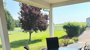 Une terrasse couverte avec une table et des chaises en verre, une clôture blanche et un arbre en arrière-plan.