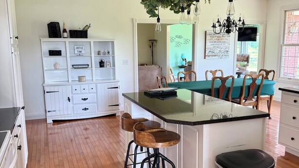 Une cuisine dotée d’un îlot central, de tabourets en bois, d’une poubelle et d’une composition végétale suspendue.