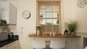 A kitchen with a wooden countertop, two white chairs, a clock, and a window with blinds.