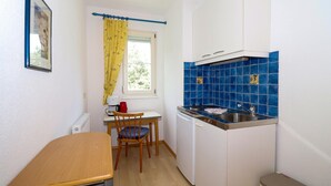 Una kitchenette compacta con estufa, lavamanos y un pequeño comedor con una silla y mesa.