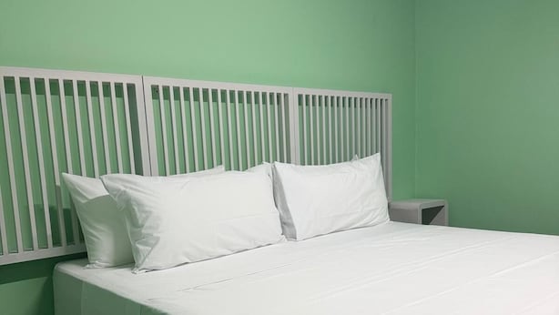 Une chambre avec un lit simple, une tête de lit blanche, des murs verts et une table de chevet marron foncé.