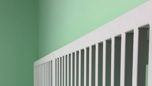 Une chambre avec une tête de lit blanche, un matelas gris et un mur vert.
