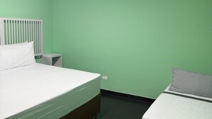 Une chambre avec deux lits, une tête de lit blanche, une table de chevet et un mur vert.