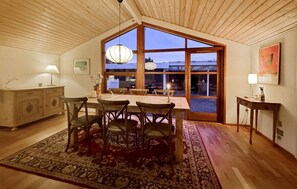 Un coin repas avec une table et des chaises en bois, un tapis et une grande fenêtre donnant sur l’extérieur.