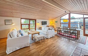 Un salon chaleureux avec un plafond en bois, un ensemble de canapés, une table à manger avec des chaises et de grandes fenêtres.