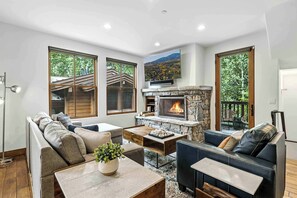 A modern living room with a stone fireplace, large windows, and a cozy seating area.