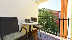 A balcony with a round table and two chairs, a small basket, and a view of a red brick building and trees. - Studio apartment 2362/160182 (Istria - Rovinj), 800m from the beach (Rovinj)