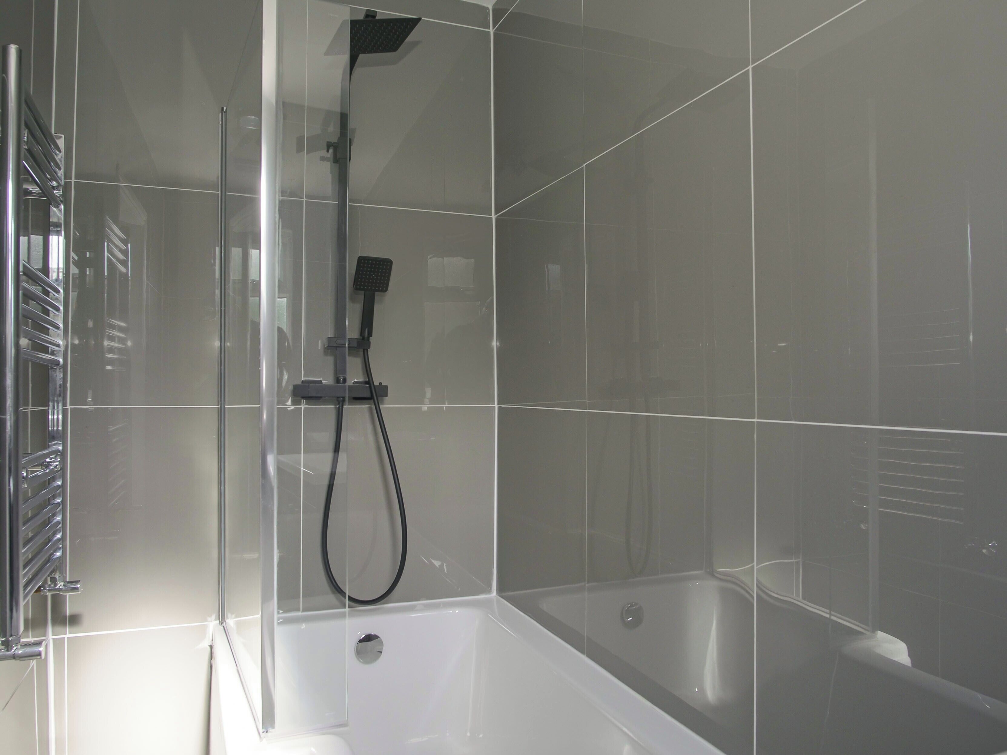 A modern shower enclosure with a handheld showerhead and a built-in bathtub.