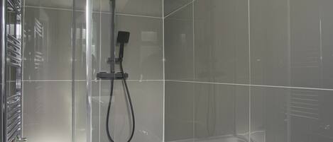 A modern shower enclosure with a handheld showerhead and a built-in bathtub.