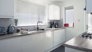 A modern kitchen with white cabinets, a black faucet, a coffee maker, and a red bag on the windowsill. - Cozy Riverside Retreat in Snodland (Snodland)