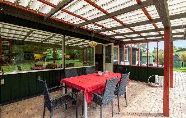 A covered patio with a table and chairs, large windows, and a view of the garden.