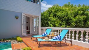 A terrace with two sun loungers, a small pool, and a white building with a balcony.