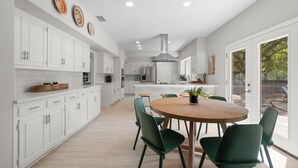 A modern kitchen with white cabinets, a central island, and a dining area with green chairs.