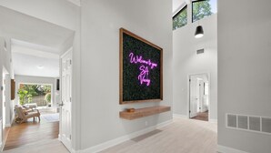 A modern hallway with a neon sign reading "Welcome to your SA Vacay."