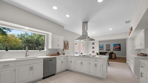 A modern kitchen with white cabinetry, a large island, and a view of the outdoors.