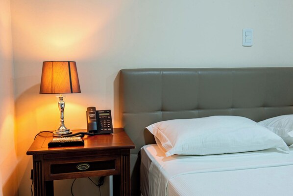 Une chambre d’hôtel comprenant un lit, une table de chevet avec une lampe, un téléphone et une prise électrique.