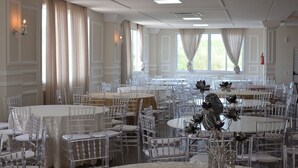 A banquet hall with multiple round tables and chairs, large windows with curtains, and wall-mounted lighting fixtures. - Hotel Cassemiro By Rede Nossa casa (Coronel Bicaco)