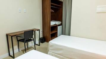 Una habitación de hotel con escritorio, dos camas, armario y una silla.