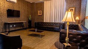 A modern living room with a black leather sofa, a coffee table, and a TV mounted on the wall. - Hotel Cassemiro By Rede Nossa casa (Coronel Bicaco)