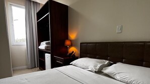 A hotel room with a large bed, a wardrobe, a bedside lamp, and a window with curtains. - Hotel Cassemiro By Rede Nossa casa (Coronel Bicaco)