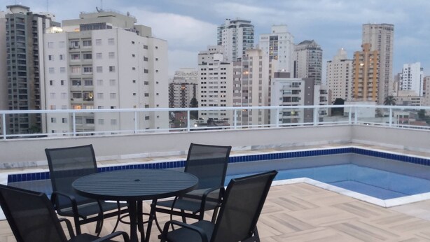 Un espace piscine aménagé sur le toit, avec une table et des chaises, le tout entouré d’une rambarde blanche.