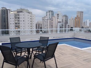 A rooftop pool area with a table and chairs, surrounded by a white railing. - Studio with balcony and wide view in Santana - SP, Jardim São Paulo subway, 12 min (São Paulo)