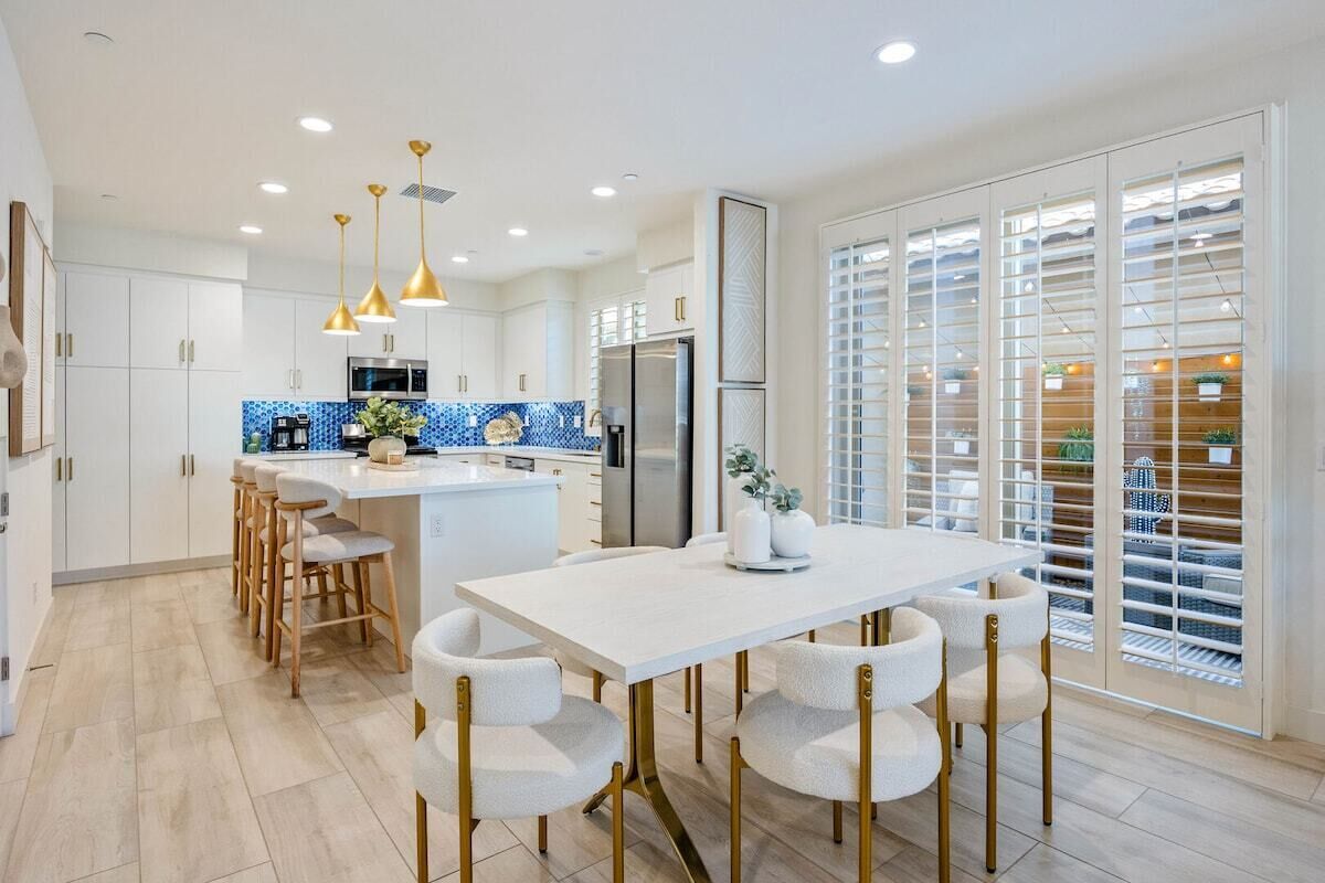A modern kitchen with a central island, bar stools, pendant lighting, and a view through a sliding glass door.