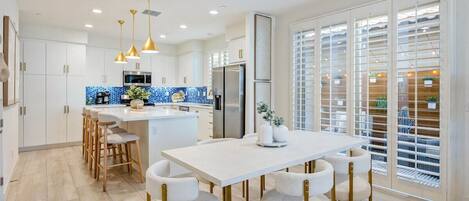 A modern kitchen with a central island, bar stools, pendant lighting, and a view through a sliding glass door.