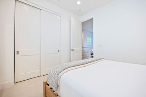 Une chambre à coucher avec un lit, une tête de lit en bois, un mur blanc et une porte donnant sur un placard.
