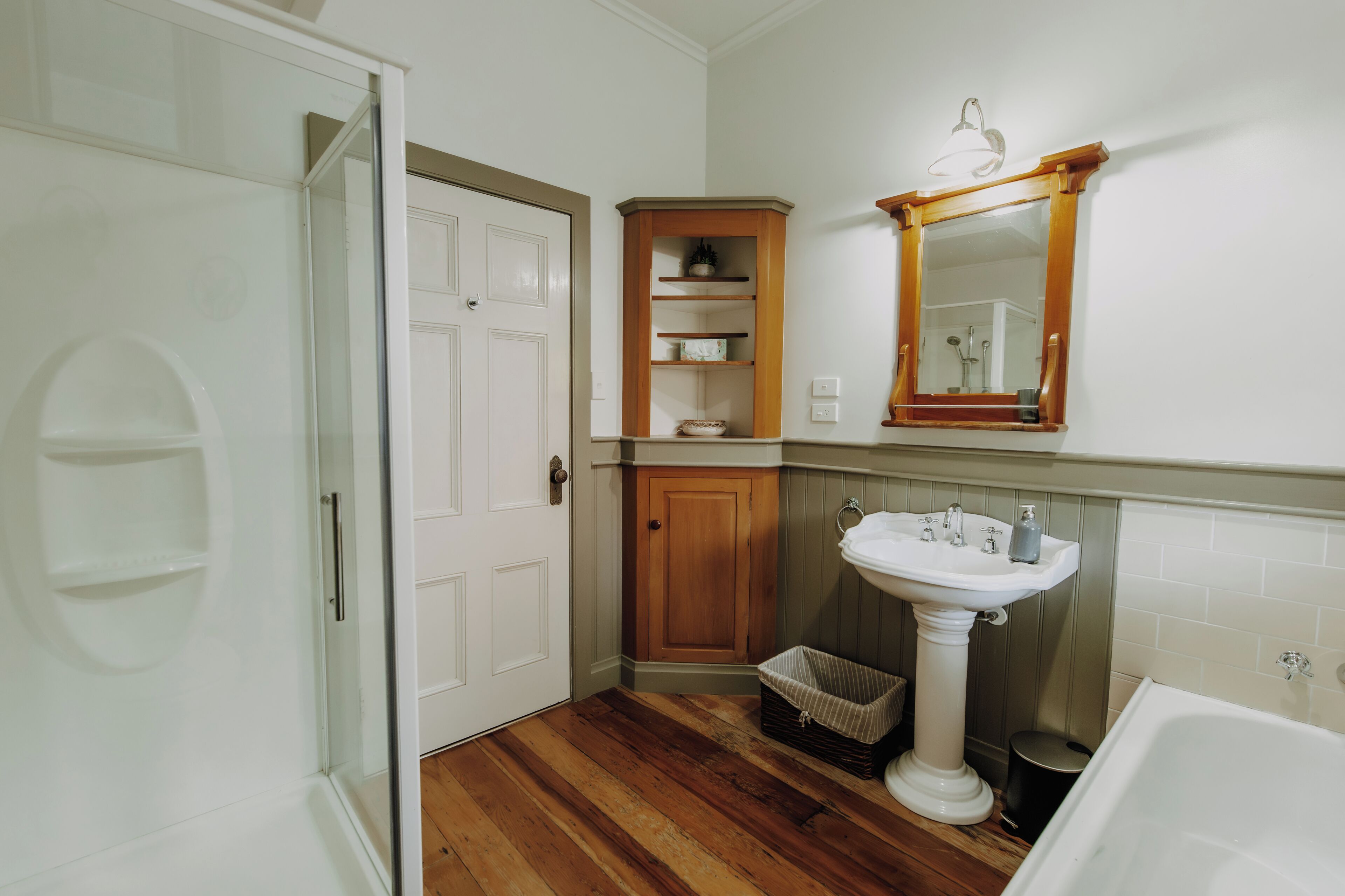 A bathroom with a wooden floor, white walls, a white sink, and a mirror above it.