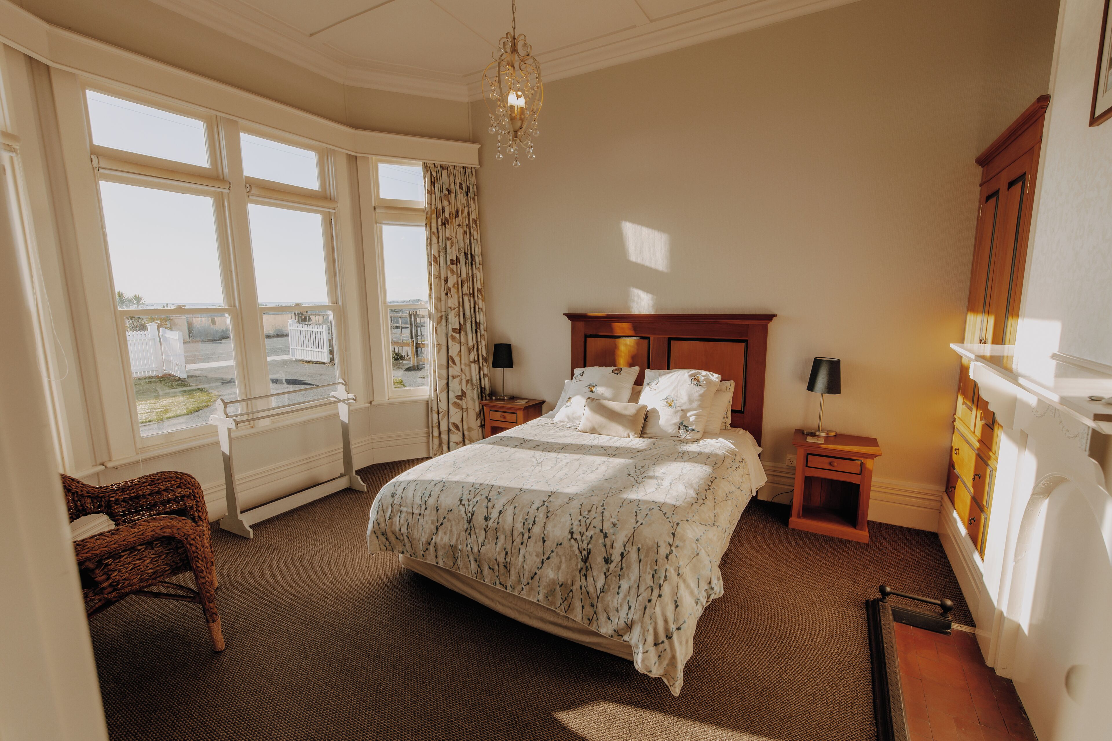 A bedroom with a large bed, a wooden nightstand, a chair, a radiator, and a view of the outside.