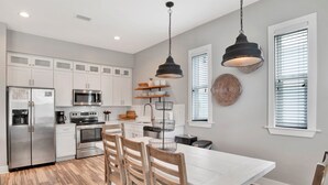 A modern kitchen with white cabinets, stainless steel appliances, and a wooden dining table. - 2 Mins to Beach | Pool View Retreat | Fully Loaded (Gulf Shores)