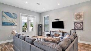 A living room with a gray sectional sofa, a flat-screen TV, and artwork on the walls. - 2 Mins to Beach | Pool View Retreat | Fully Loaded (Gulf Shores)