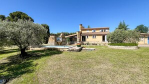 A two-story house with a swimming pool, surrounded by a well-maintained lawn and trees.