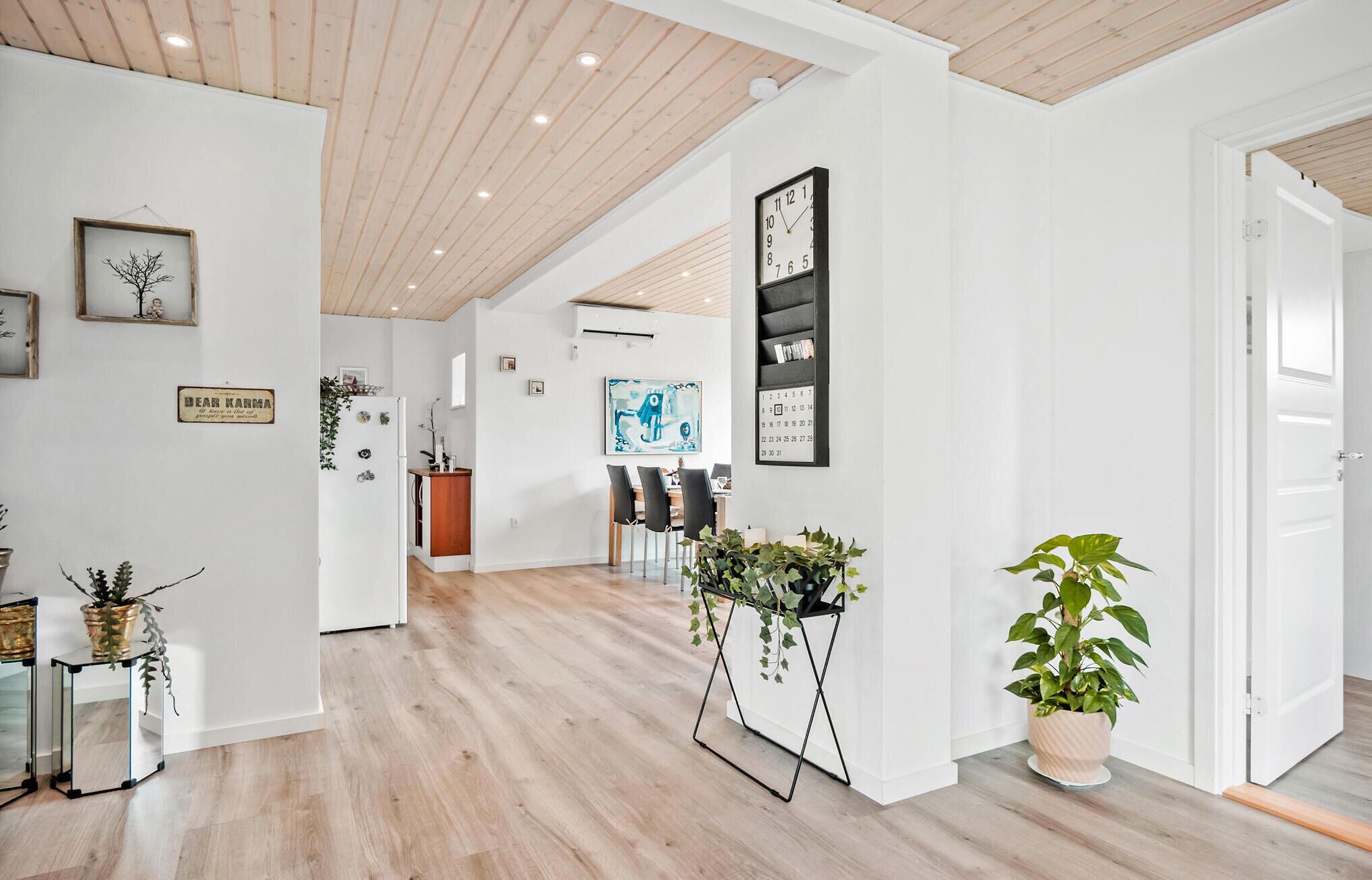 A spacious hallway with wooden flooring, a dining area with chairs and a table, and a kitchen area with a refrigerator and a sink.