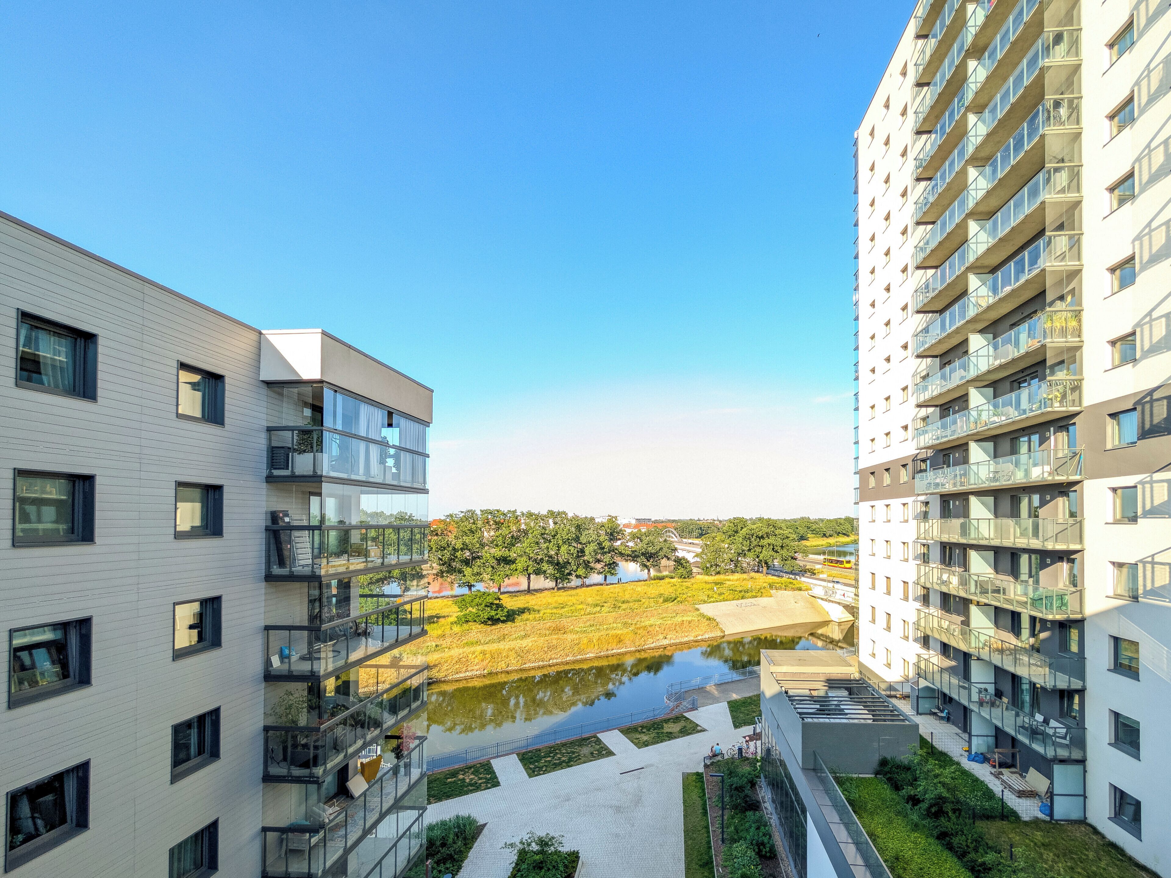 Un edificio moderno de apartamentos con varios balcones, un patio con un pequeño estanque y vistas a un parque distante.