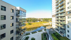 A modern apartment building with multiple balconies, a courtyard with a small pond, and a view of a distant park. - 6th Floor Studio with the River View (Wrocław)