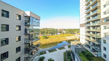 Un edificio moderno de apartamentos con varios balcones, un patio con un pequeño estanque y vistas a un parque distante.